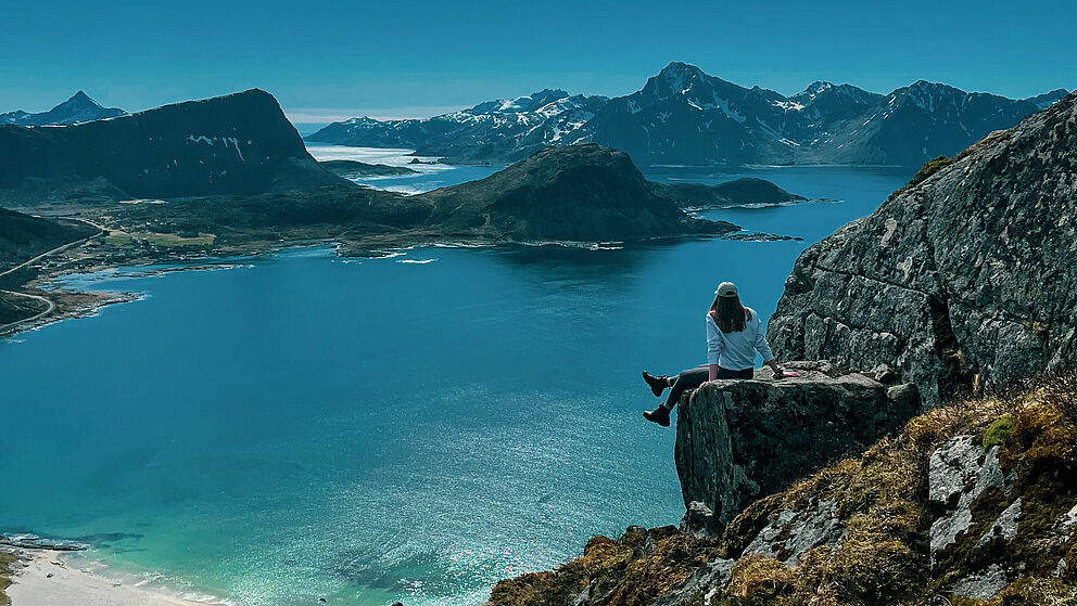 Eine junge Frau sitzt auf einer Klippe ber dem Meer in einer idyllischen Landschaft.